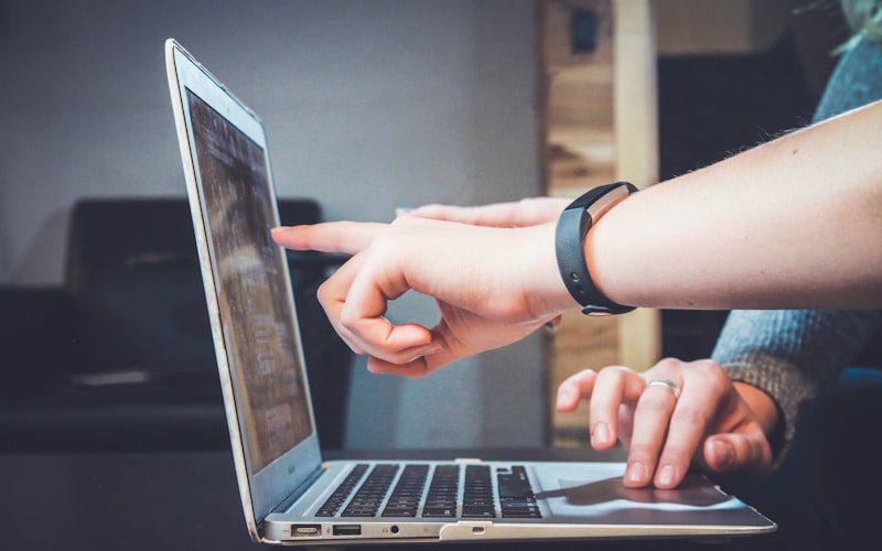 A person pointing at a laptop screen while another person types
