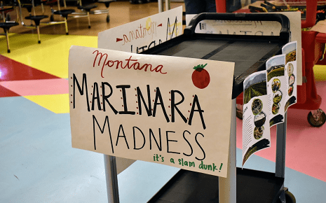 Hand-lettered Montana Marinara Madness sign on a cart in a school cafeteria