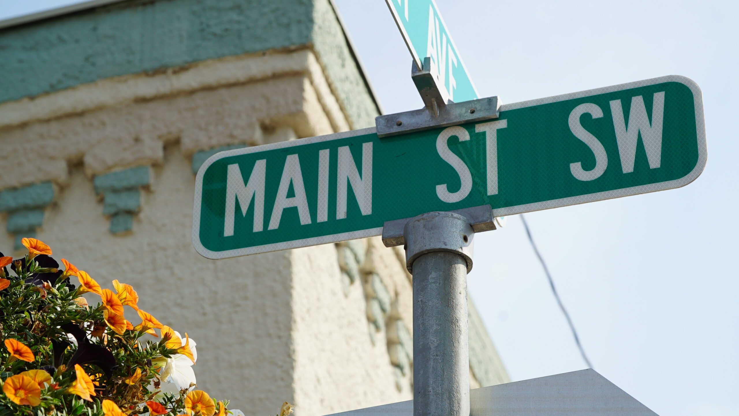 Main Street SW street sign in downtown Ronan, Montana, with flower baskets and a historic building behind