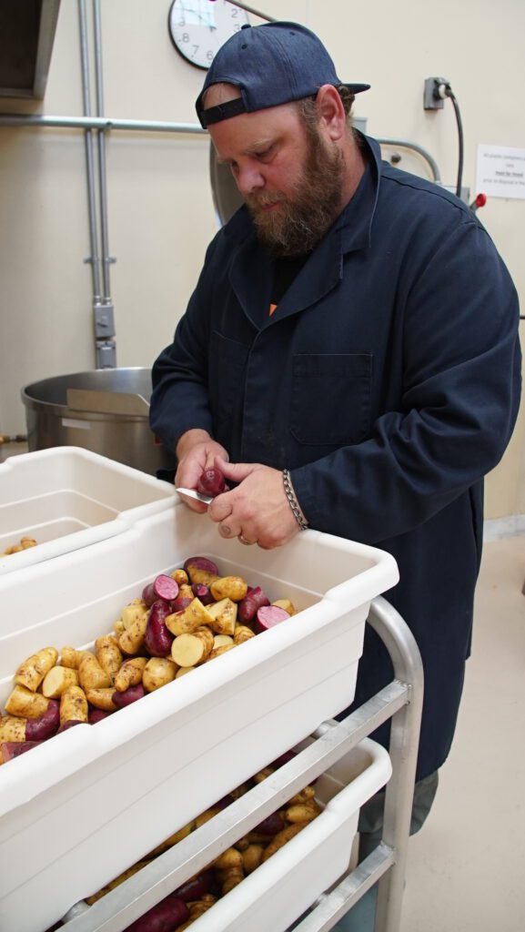 Worker in the MMFEC processing facility cutting red and yellow potatoes into bins