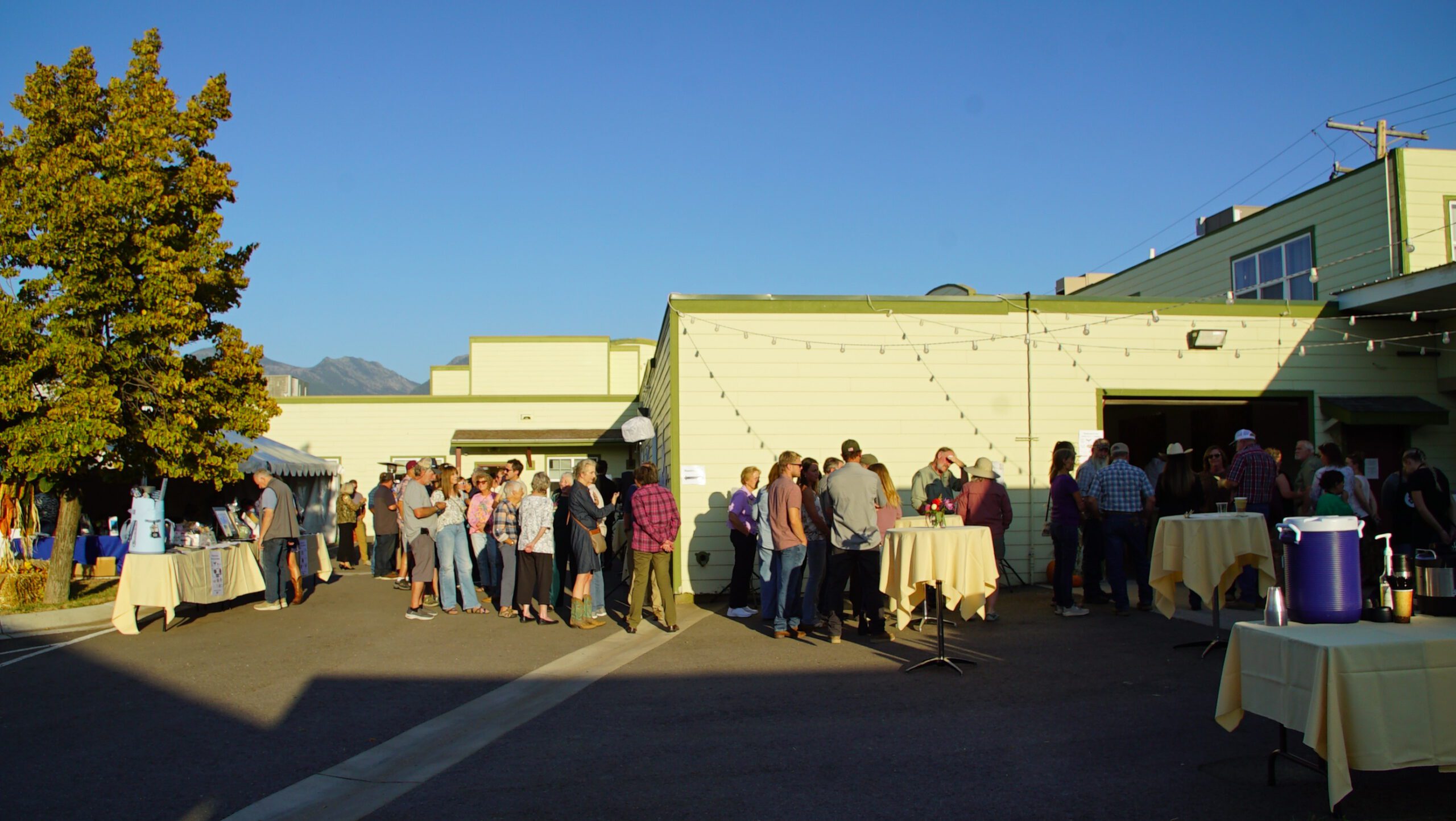 Guests lined up at an outdoor evening event with string lights and the Mission Mountains in the background