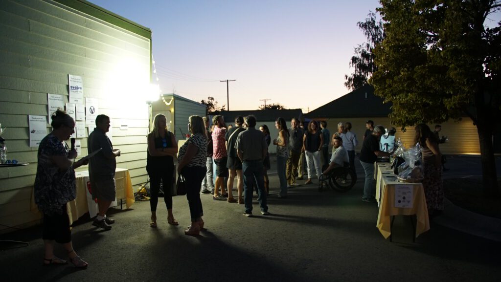 Crowd of guests mingling at dusk during the Harvest on Main event, with dessert tables and string lights