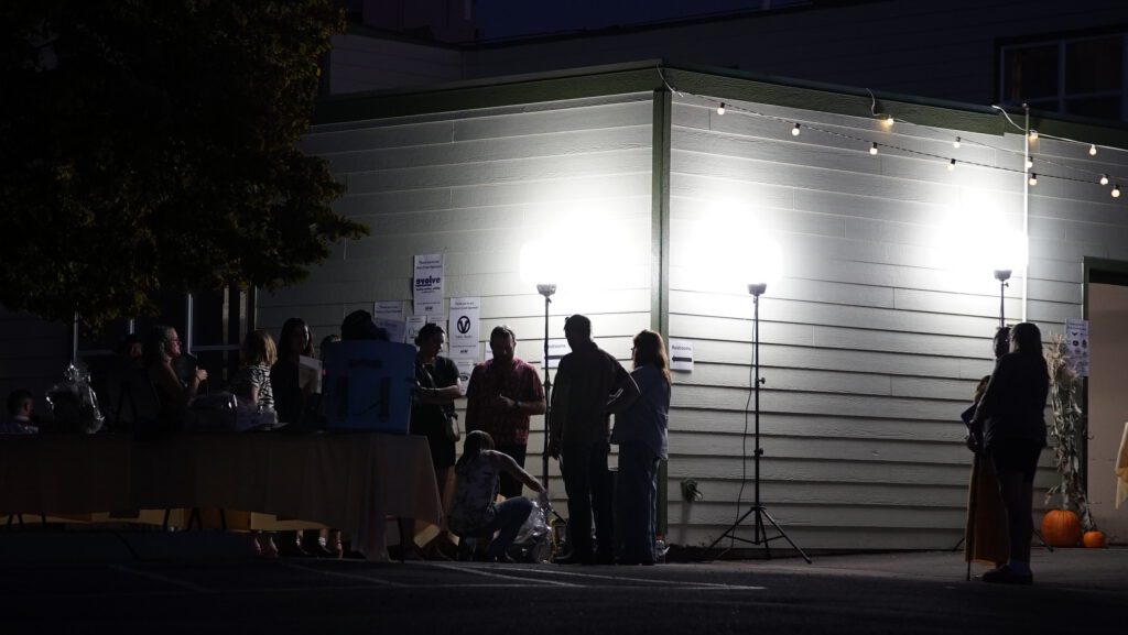 Guests at an outdoor evening check-in table lit by string lights and floodlights at the Harvest on Main event